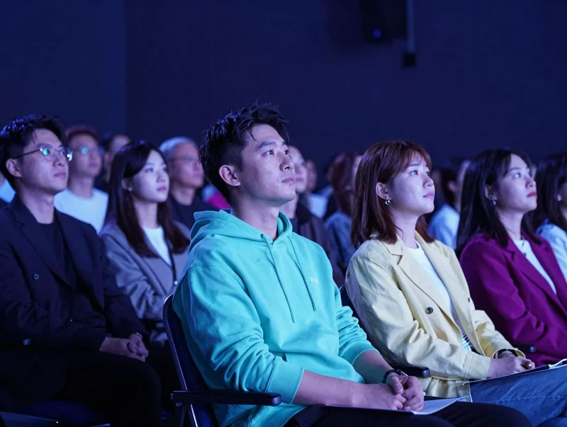 An attentive audience in a modern auditorium bathed in electric blue stage light
