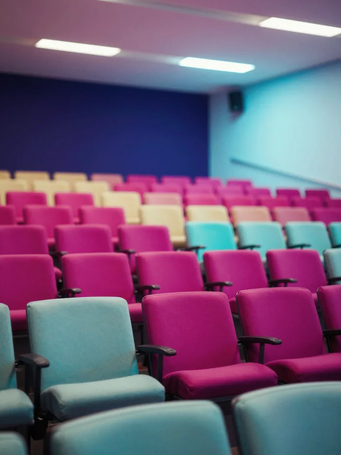 A packed modern conference auditorium lit in vivid magenta and cyan stage light