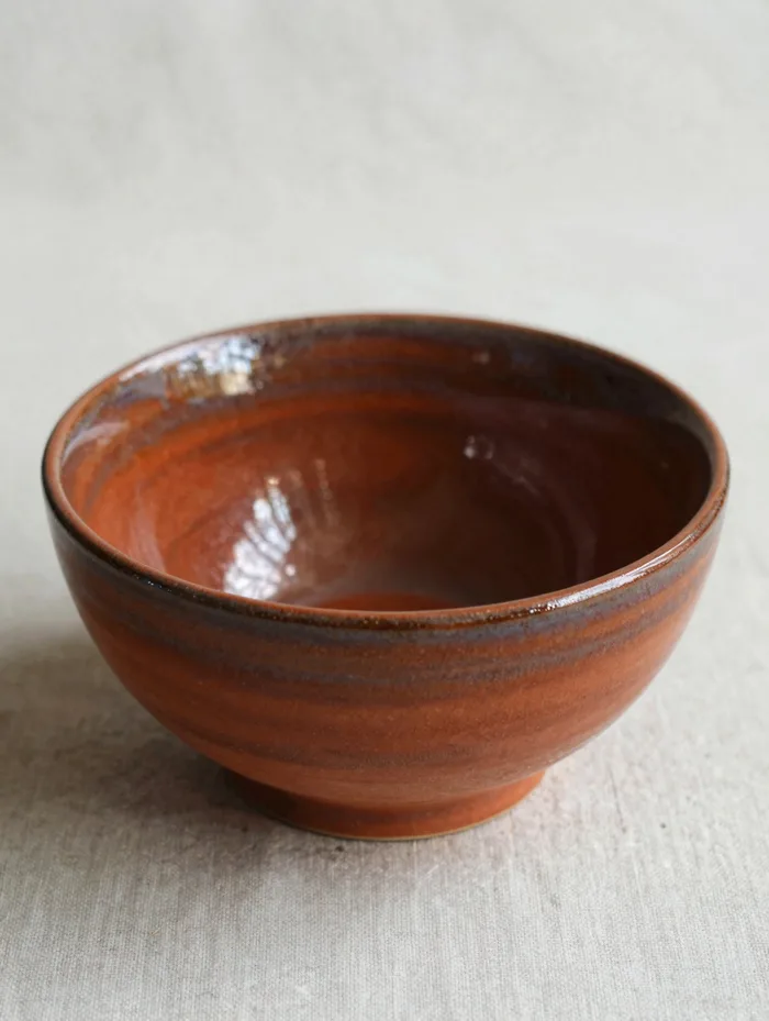 A ripple bowl in warm terracotta glaze on linen, artisanal ceramics