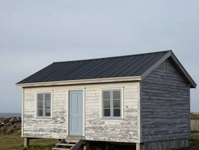 A low-slung coastal house in weathered timber against a grey sky, calm architectural photography