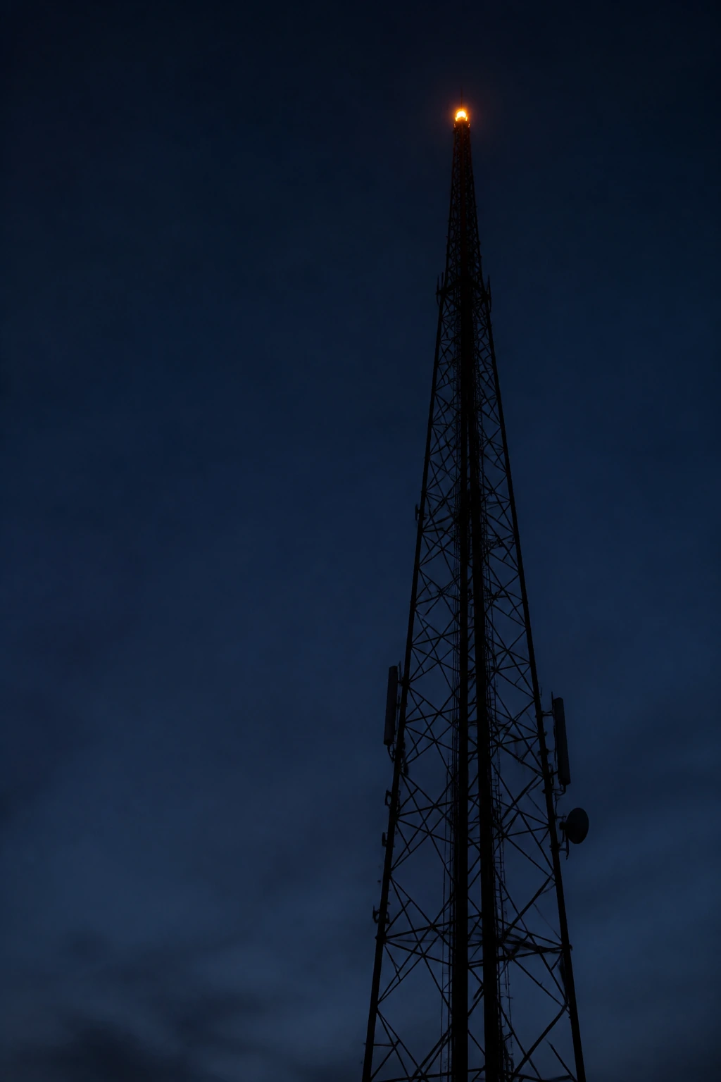 A lattice transmitter mast against a deep dusk sky with a single warning light