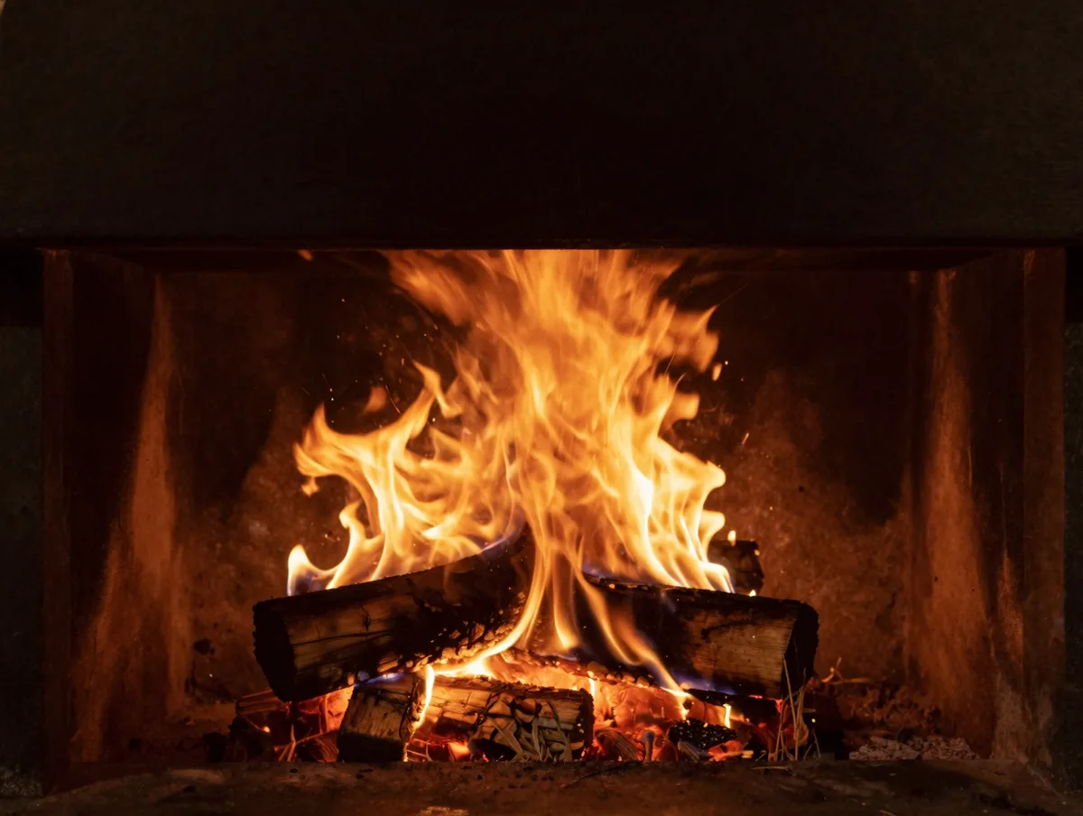 A glowing wood-fired restaurant hearth with flames and embers, deep amber light