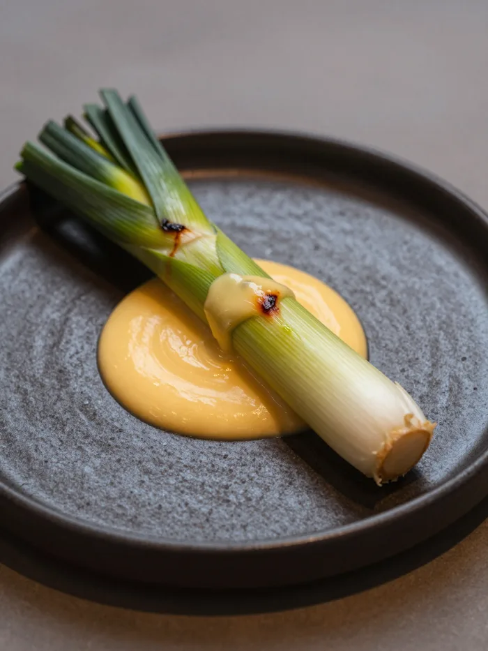 A charred whole leek with ember cream on dark ceramic, moody restaurant light