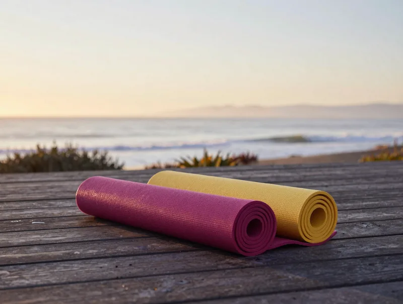 A serene coastal yoga deck at sunrise overlooking the Pacific, a single rolled mat, warm dawn light